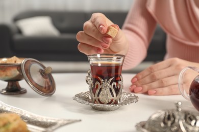 Woman adding sugar to delicious Turkish tea at white table, closeup