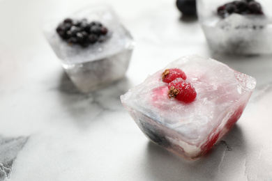 Ice cubes with different berries and mint on white marble table, closeup