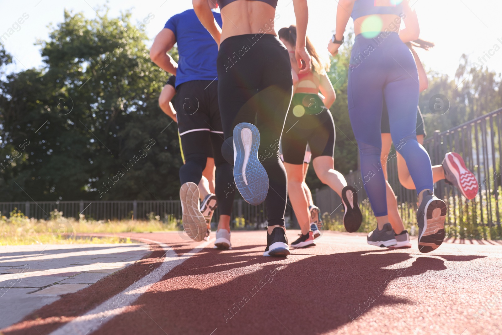 Photo of Group of people running at stadium on sunny day, back view