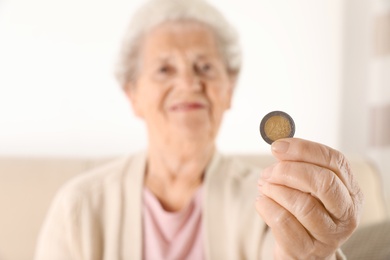 Elderly woman holding coin indoors, focus on hand