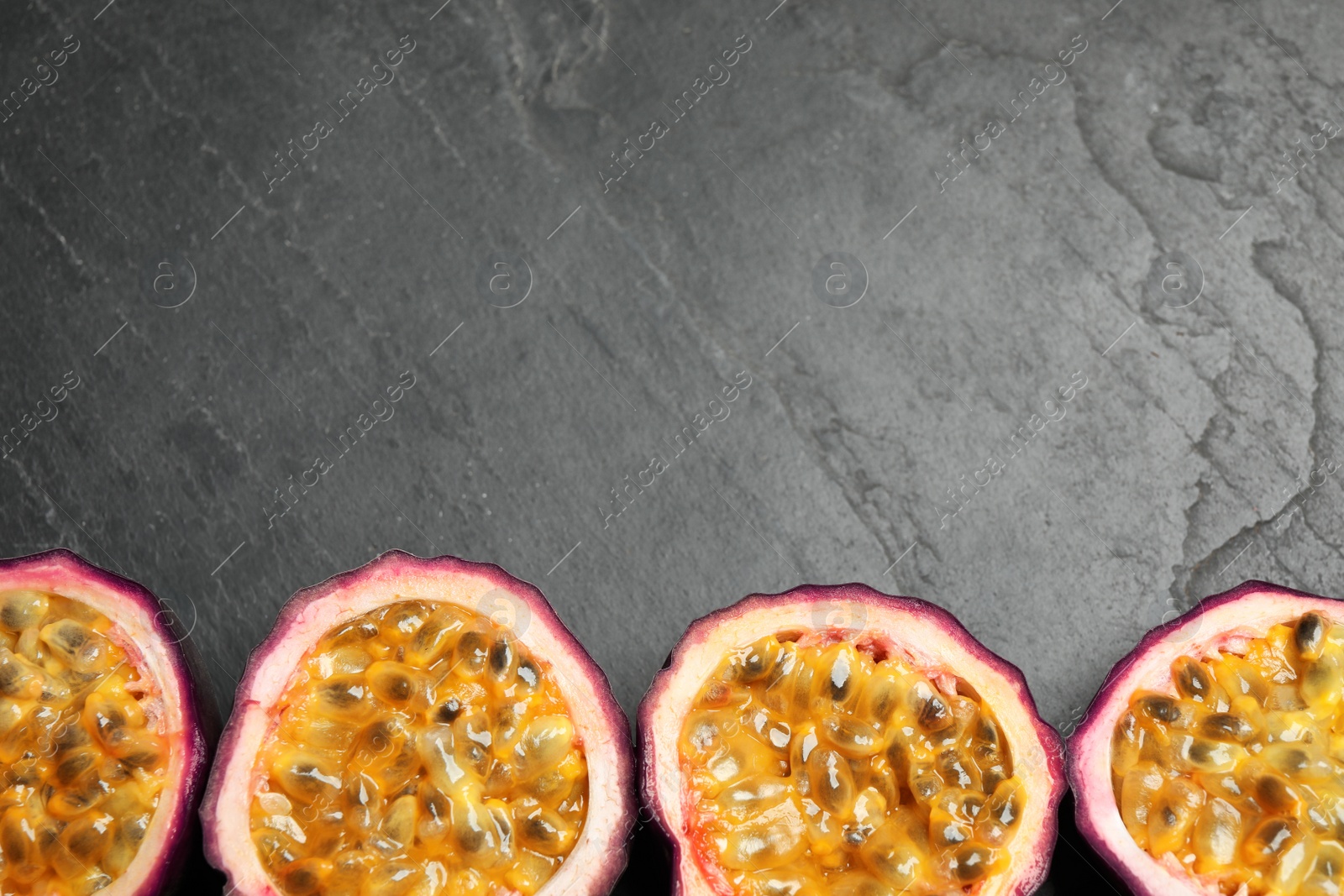 Photo of Halves of passion fruits (maracuyas) on black slate table, flat lay. Space for text