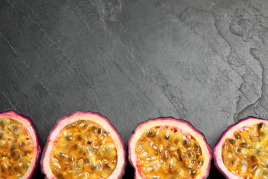 Photo of Halves of passion fruits (maracuyas) on black slate table, flat lay. Space for text