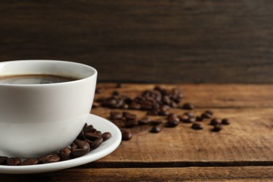 Photo of Cup of aromatic coffee and beans on wooden table. Space for text