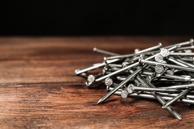 Photo of Pile of metal nails on wooden background, closeup. Space for text