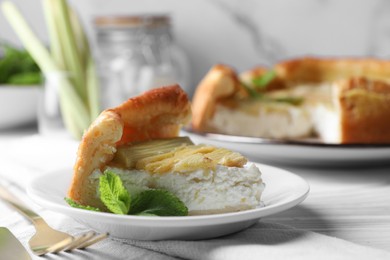 Piece of freshly baked rhubarb pie with cream cheese, mint leaves and cutlery on white wooden table, closeup