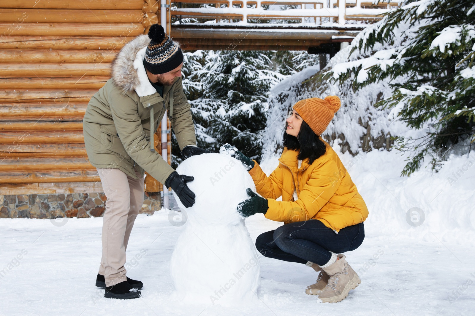 Photo of Happy couple making snowman together outdoors. Winter vacation