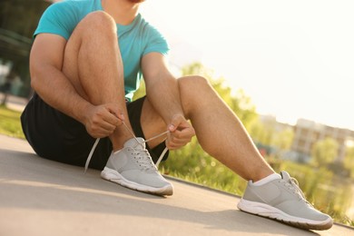 Photo of Man tying shoelaces before running outdoors on sunny day, closeup