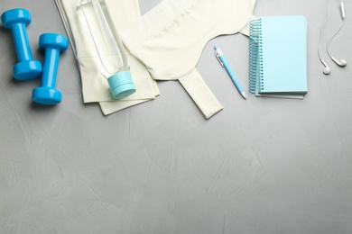 Photo of Flat lay composition with sportswear, notebook and dumbbells on grey background, space for text. Gym workout plan