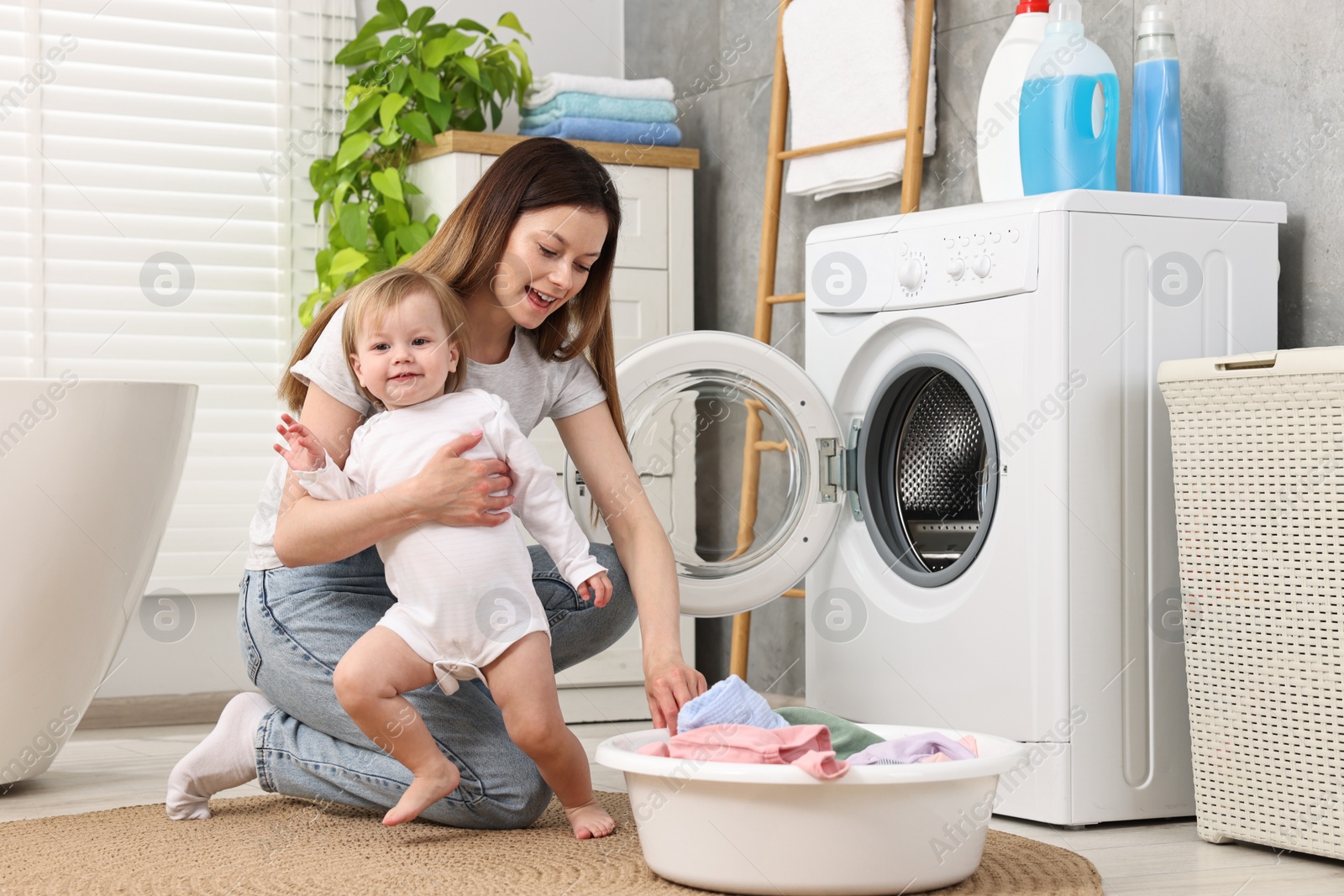 Photo of Happy mother with her daughter washing baby clothes in bathroom