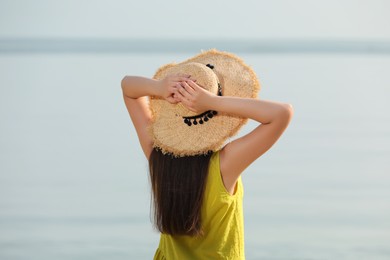 Photo of Beautiful young woman wearing straw hat on beach, back view. Stylish headdress