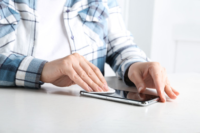 Photo of Woman cleaning mobile phone with cotton pad at white table indoors, closeup