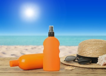 Image of Bottles of skin sun protection products and beach accessories on wooden table against seascape. Space for design