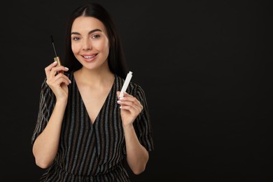 Photo of Beautiful young woman with mascara on black background, space for text