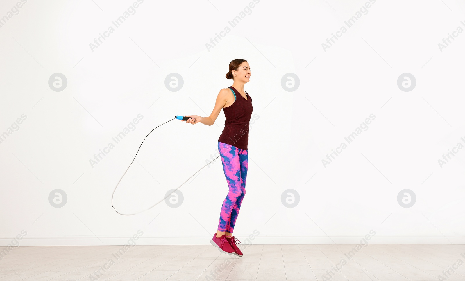 Photo of Young sportive woman training with jump rope in light room