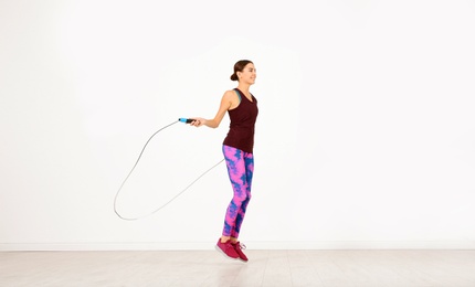 Young sportive woman training with jump rope in light room