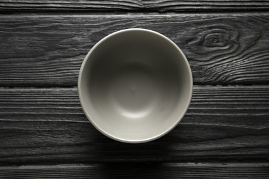 Photo of Stylish empty ceramic bowl on black wooden table, top view. Cooking utensil