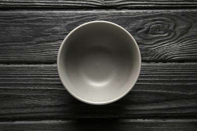 Stylish empty ceramic bowl on black wooden table, top view. Cooking utensil