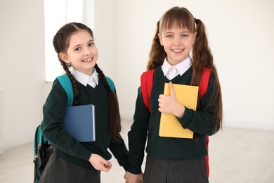 Photo of Portrait of cute girls in school uniform with backpacks and books indoors