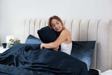 Photo of Young woman hugging pillow in comfortable bed with dark blue linens at home