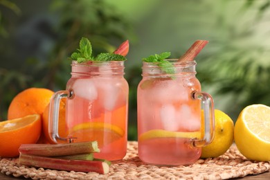 Photo of Mason jars of tasty rhubarb cocktail with citrus fruits on table outdoors