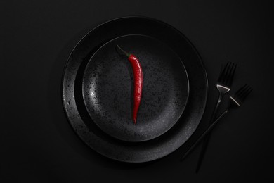 Photo of Stylish table setting. Plates, cutlery and red chilli pepper on black background, top view