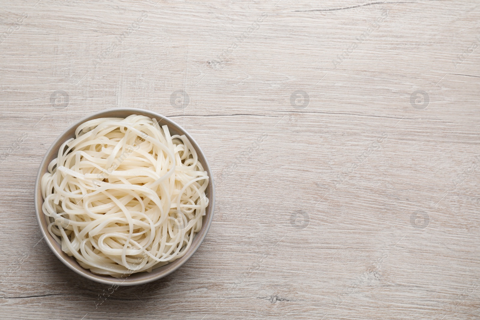 Photo of Bowl of tasty cooked rice noodles on white wooden table, top view. Space for text