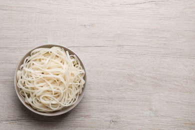 Bowl of tasty cooked rice noodles on white wooden table, top view. Space for text