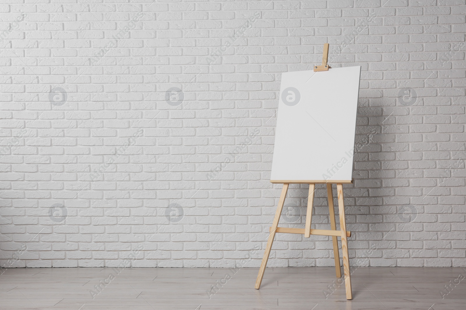 Photo of Wooden easel with blank canvas near white brick wall indoors. Space for text