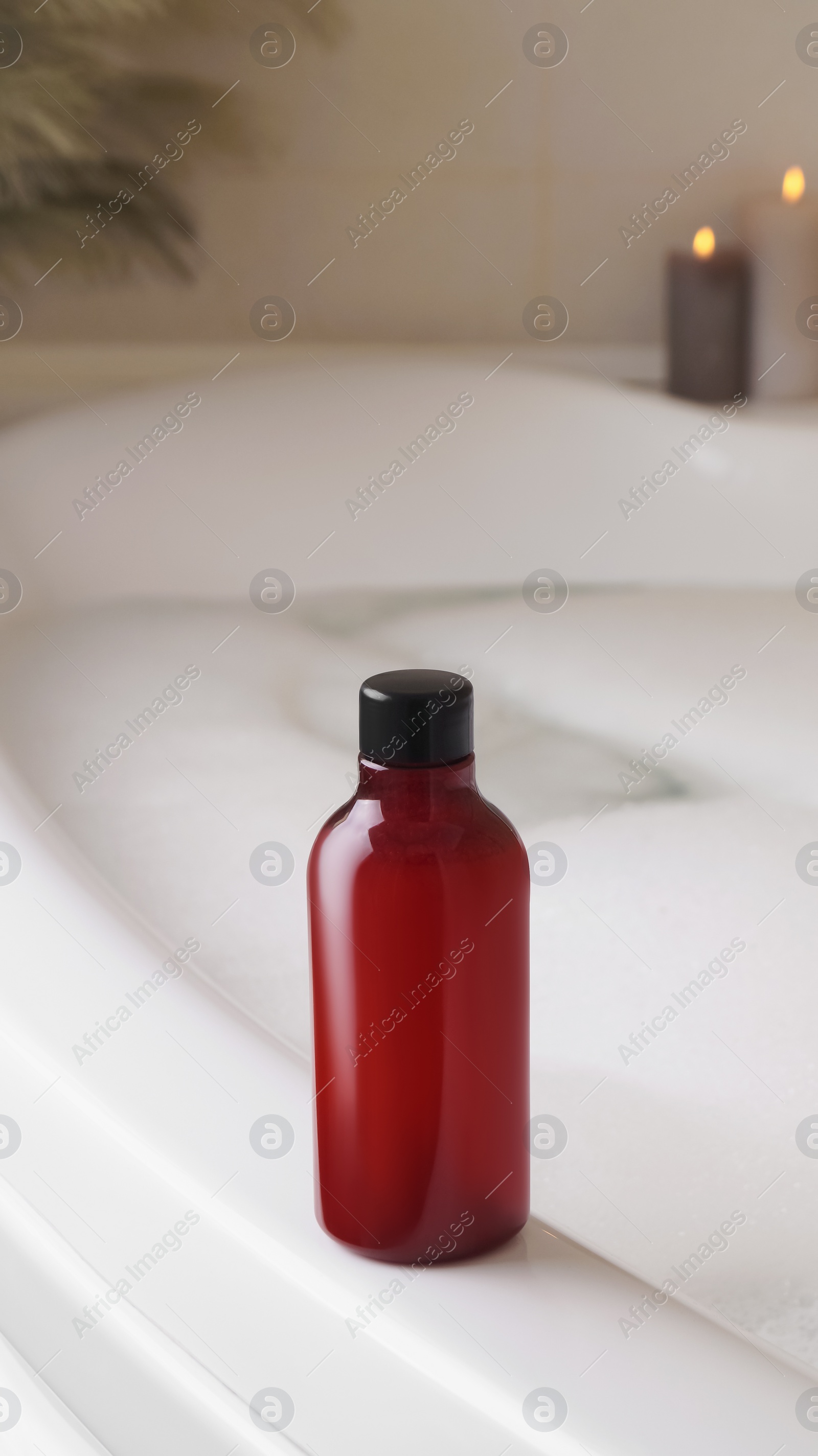 Red bottle of bubble bath on tub indoors Photo of Red bottle of bubble bath on tub indoors