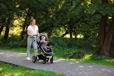 Photo of Happy nanny with cute little boy in stroller walking in park, space for text