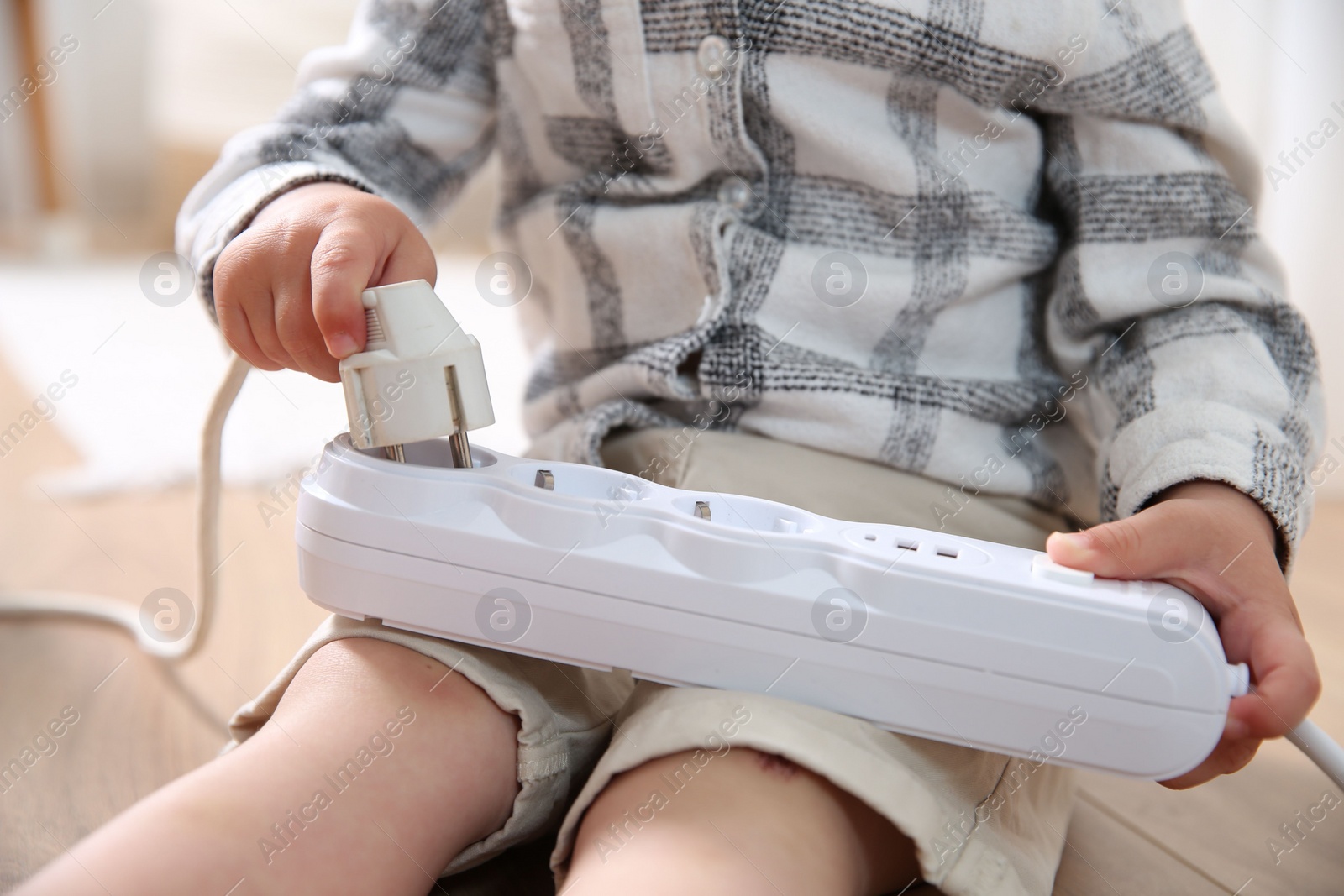 Photo of Little child playing with power strip and plug on floor indoors, closeup. Dangerous situation