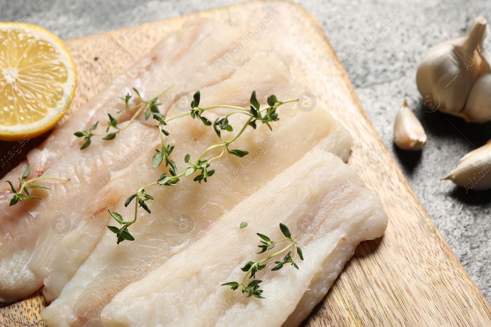 Photo of Raw cod fish, microgreens and lemon on grey textured table, closeup