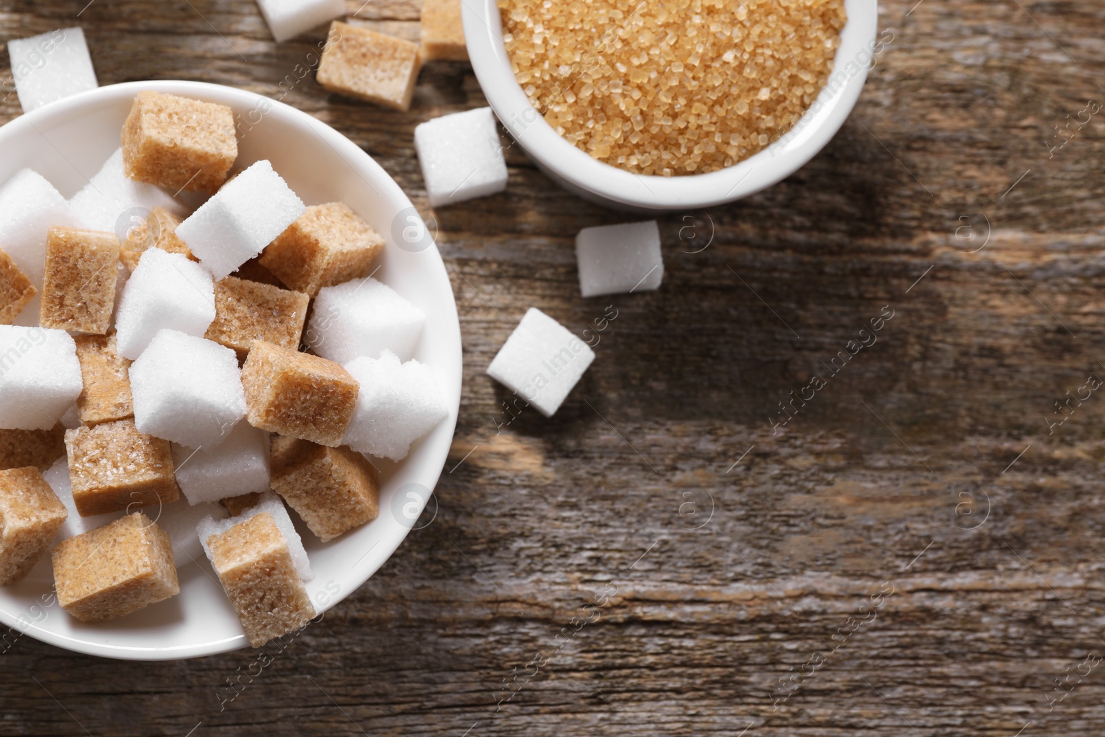 Photo of Different types of sugar in bowls on wooden table, flat lay. Space for text