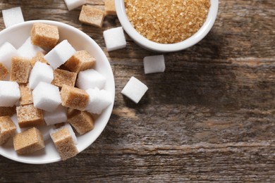 Photo of Different types of sugar in bowls on wooden table, flat lay. Space for text