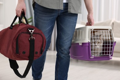 Photo of Travel with pet. Man holding carrier with cute cat and bag at home, closeup