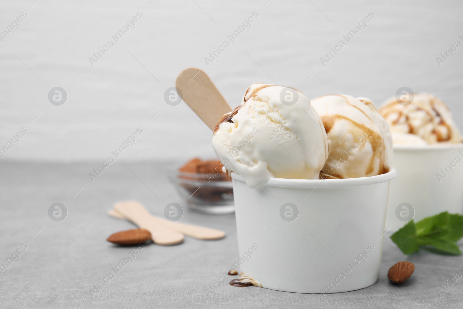 Photo of Scoops of ice cream with caramel sauce in paper cup on light grey table, closeup. Space for text