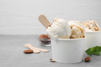 Photo of Scoopsice cream with caramel sauce in paper cup on light grey table, closeup. Space for text