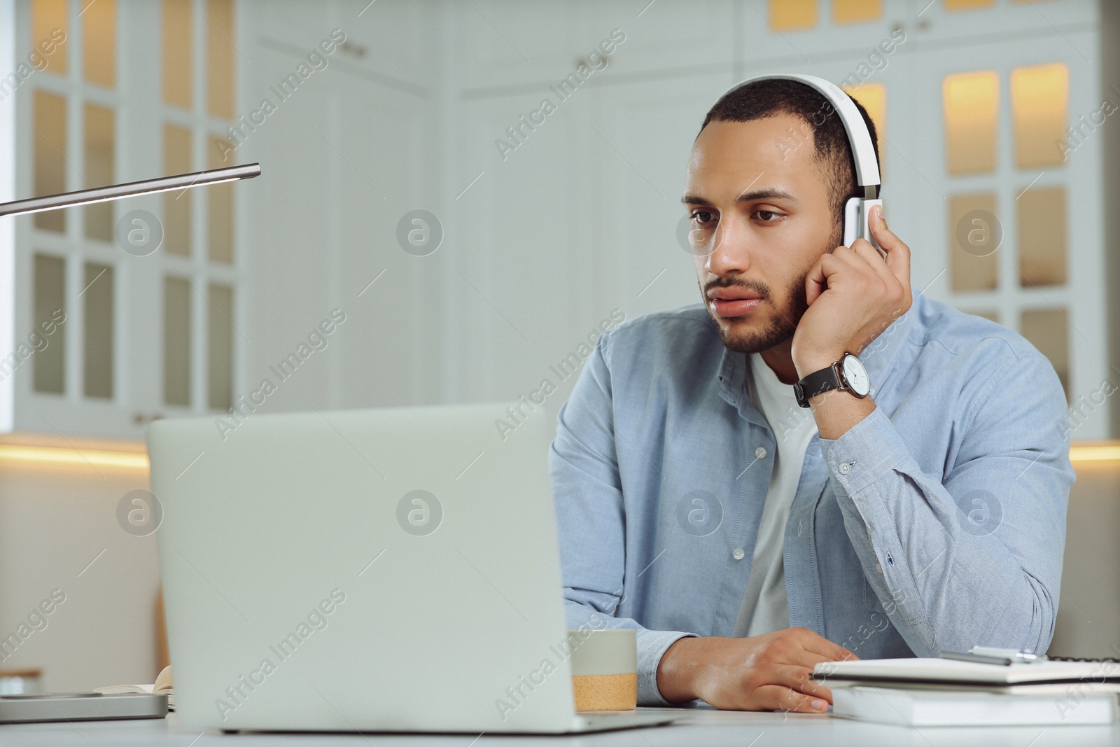 Photo of Young man with headphones working on laptop at desk in kitchen. Home office