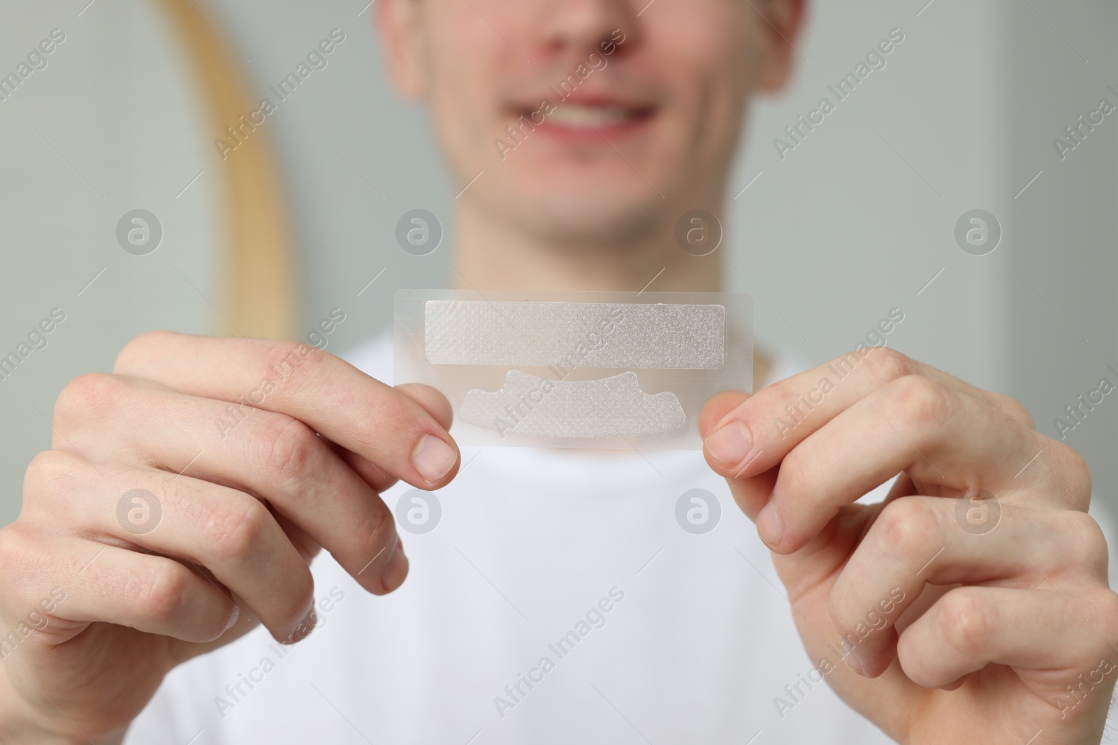 Photo of Young man with whitening strips indoors, closeup