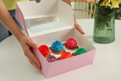 Woman with box of delicious colorful cupcakes at white table indoors, closeup