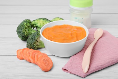 Bowl with healthy baby food, spoon and ingredients on white wooden table