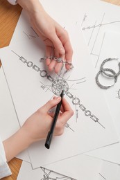 Jeweler drawing sketch of elegant bracelet on paper at wooden table, top view