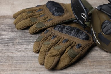 Photo of Tactical gloves and headphones on wooden table, closeup. Military training equipment