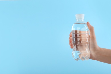 Woman holding plastic bottle with water on color background. Space for text