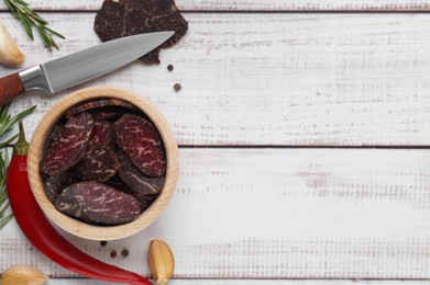 Photo of Slices of delicious beef jerky and ingredients on white wooden table, flat lay. Space for text