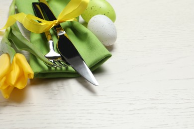 Cutlery set, eggs and beautiful flower on white wooden table, closeup with space for text. Easter celebration