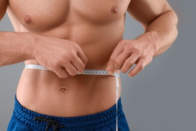 Photo of Athletic man measuring waist with tape on grey background, closeup. Weight loss concept