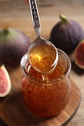 Photo of Tasty fig jam flowing down into glass jar and fresh fruits on table, closeup