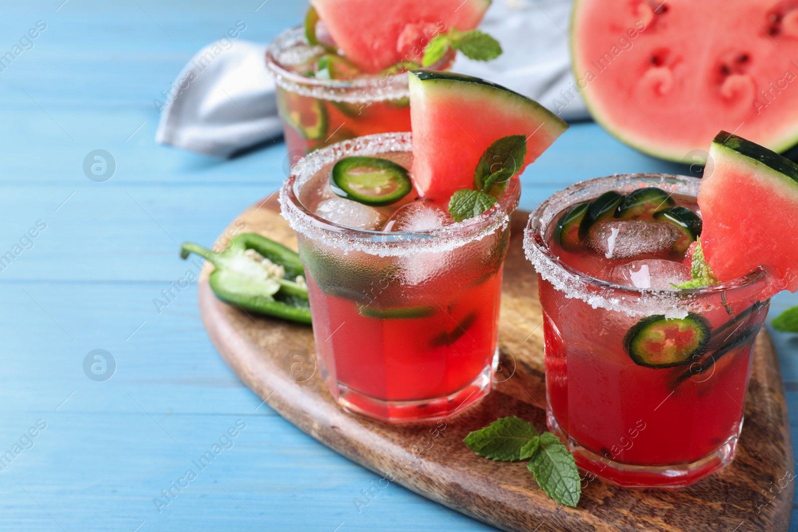 Photo of Glasses of spicy cocktail with jalapeno and mint on light blue wooden table. Space for text