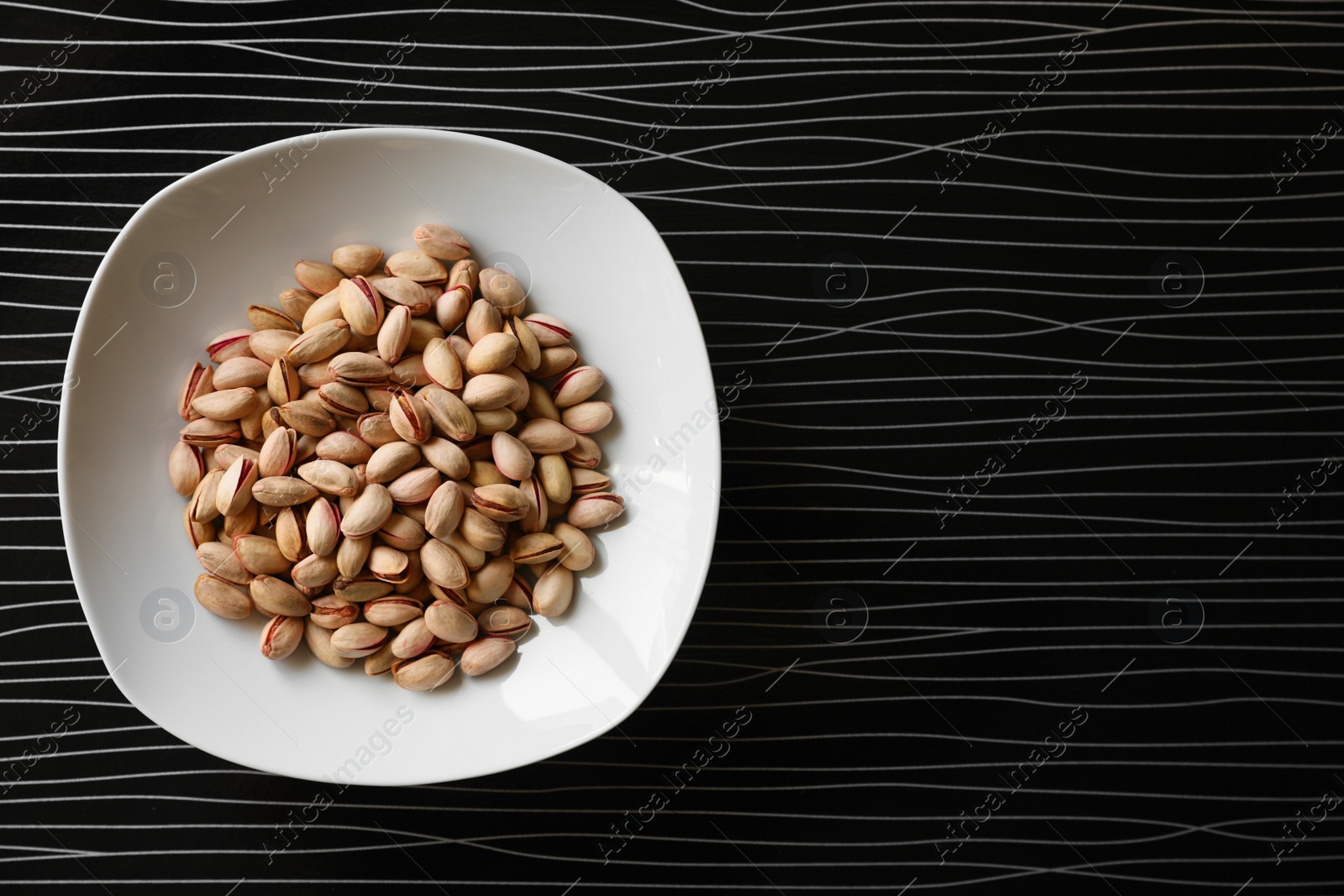 Photo of Many tasty pistachios on black table, top view. Space for text